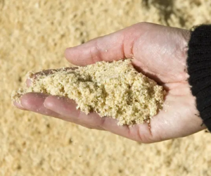 A hand holding wood pellets with a background of chopped wood logs